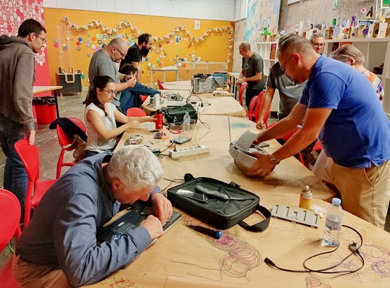 Persoas ao redor dunhas mesas longas reparando distintos aparellos electrónicos