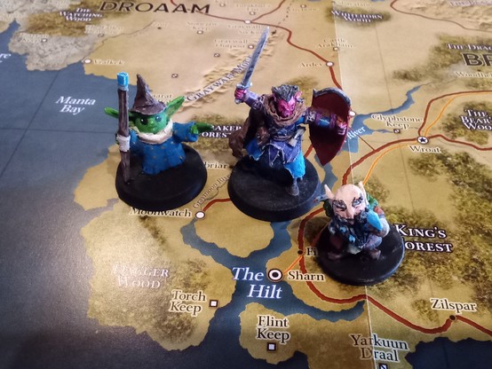 Tres miniaturas de xogos de rol: un guerreiro hobgoblin, un mago trasno e un explorador gnomo sobre un mapa de Eberron.
