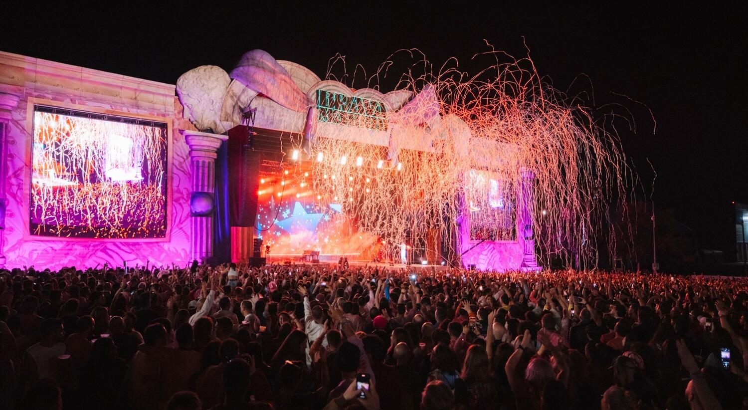 Macro festival con cheo de público entorno a un escenario con luces